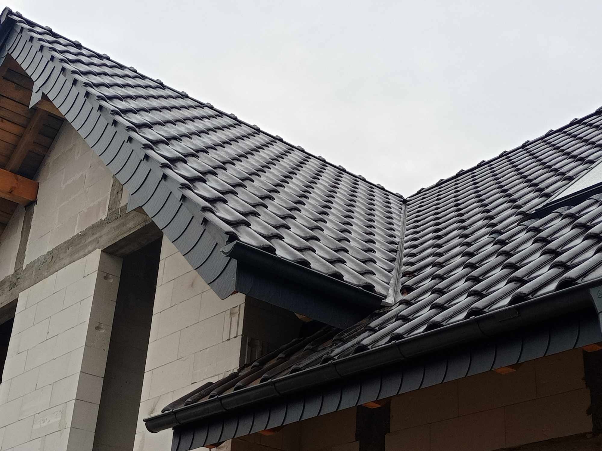 Nowy, ciemnoszary dach z dachówki ceramicznej na budynku w trakcie budowy, widoczne rynny i surowa konstrukcja z bloczków.