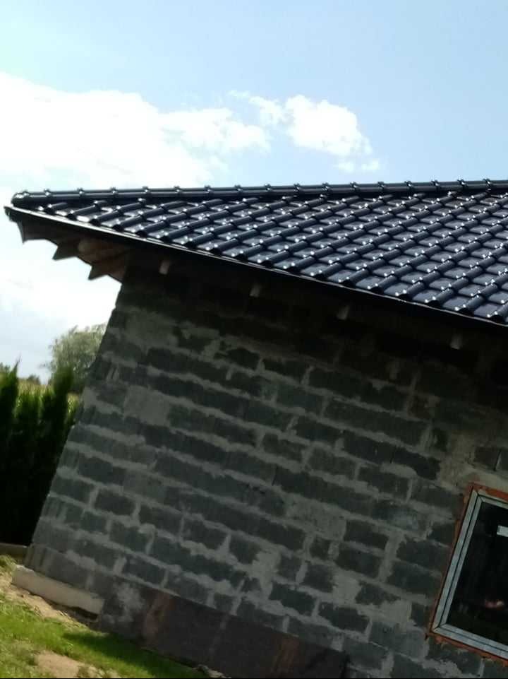 Nowy, czarny dach z dachówki ceramicznej na budynku w trakcie budowy, widok z dołu, błękitne niebo w tle.