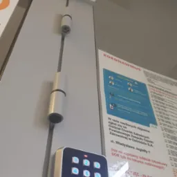 Kamera monitoringu kopułkowa Dahua, czytnik kodów z podświetlaną klawiaturą i czujnik ruchu zamontowane na ścianie wewnątrz budynku, obok plakatu informacyjnego o koronawirusie.