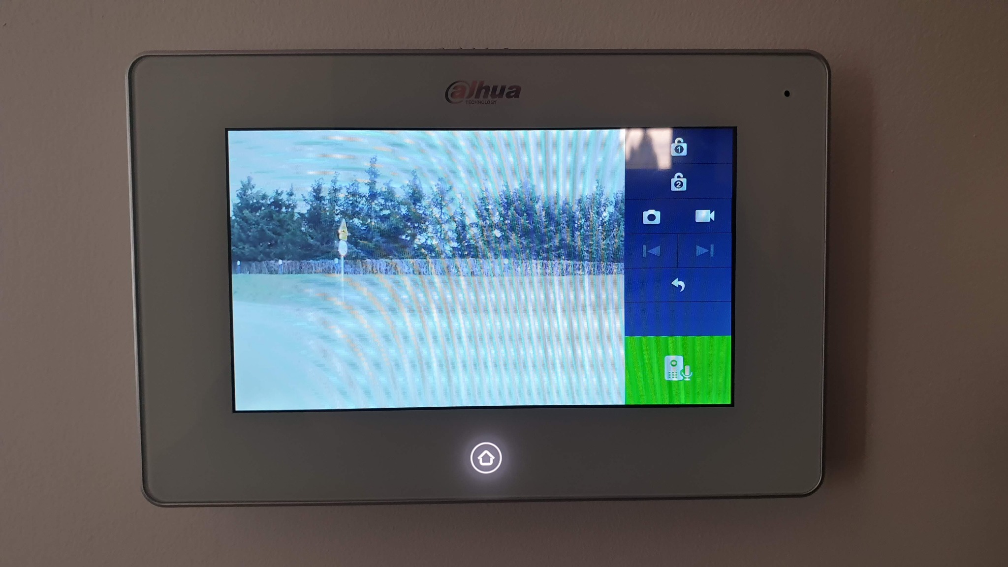 Ekran wideodomofonu Dahua zamontowanego na ścianie, wyświetlający obraz z kamery na zewnątrz, z widocznymi ikonami sterowania interfejsem.