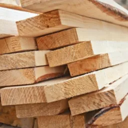 Stos jasnych, świeżo przetartych desek ułożonych warstwami, widoczne słoje drewna i drobne nierówności powierzchni.