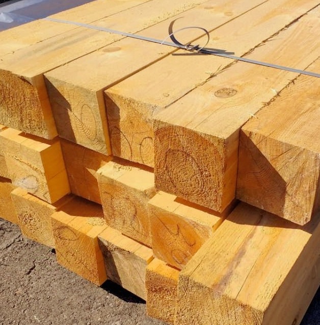 Stos świeżo przetartej, jasnej tarcicy budowlanej, związanej metalową taśmą, z widocznymi słojami drewna.