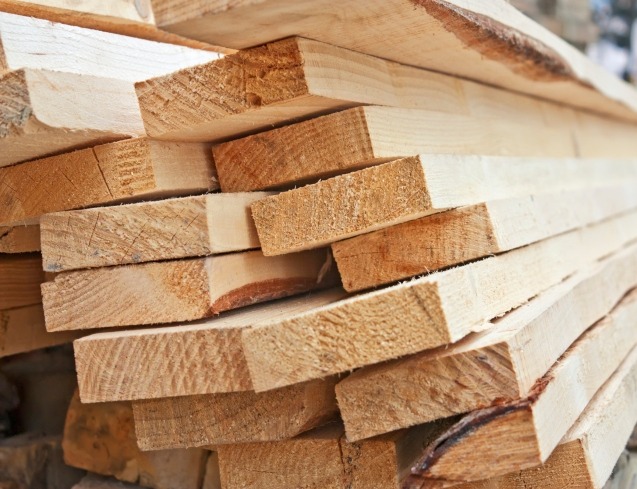 Stos jasnych, świeżo przetartych desek ułożonych warstwami, widoczne słoje drewna i drobne nierówności powierzchni.