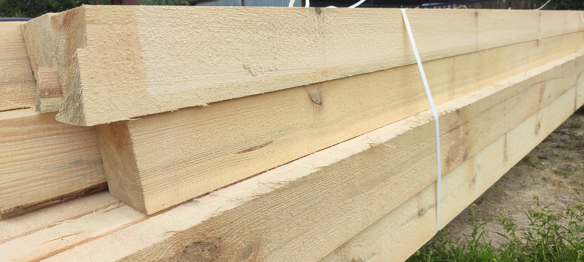 Stos świeżo przetartej, jasnej tarcicy budowlanej, związanej białym sznurkiem, z widocznymi słojami drewna i drobnymi niedoskonałościami.