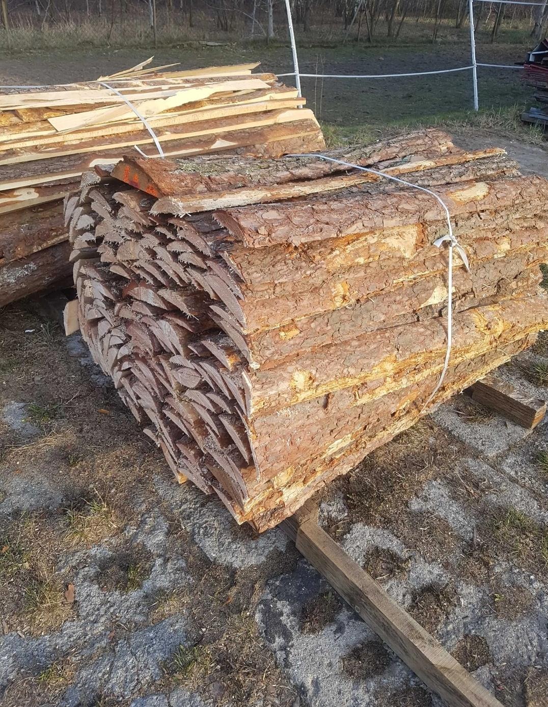 Stosy kory drzewnej związanej sznurkiem, leżące na drewnianych belkach na zewnątrz.