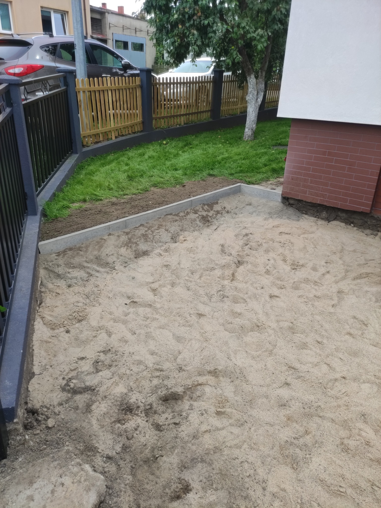 Przygotowany teren pod przyszłą kostkę brukową z obrzeżami, piaskiem i częściowo wyrównaną powierzchnią w ogrodzie.