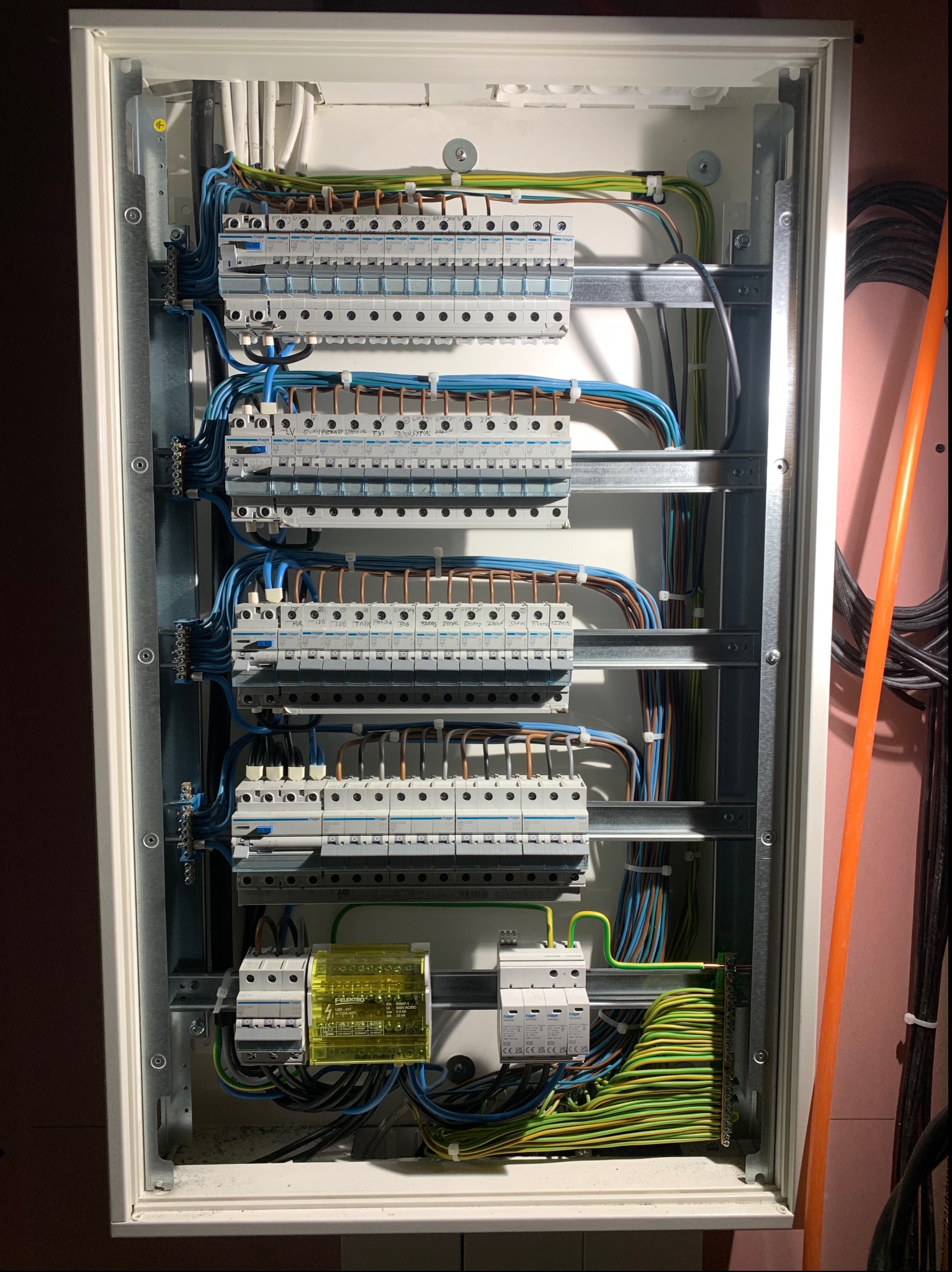 Otwarta skrzynka rozdzielcza z zamontowanymi bezpiecznikami Hager, widoczne kable w różnych kolorach i metalowe szyny montażowe.