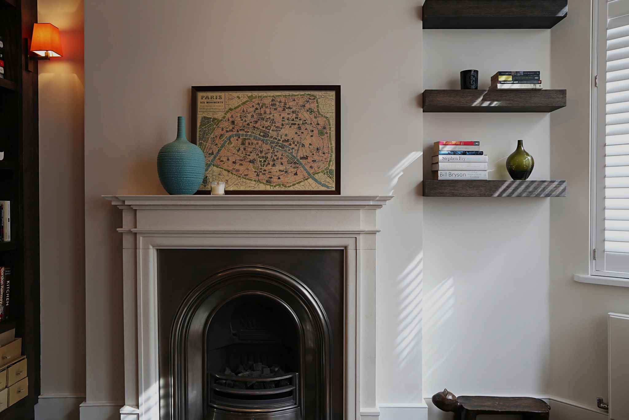 Salon z kominkiem pod mapą Paryża i pływającymi półkami z książkami oraz dekoracjami.