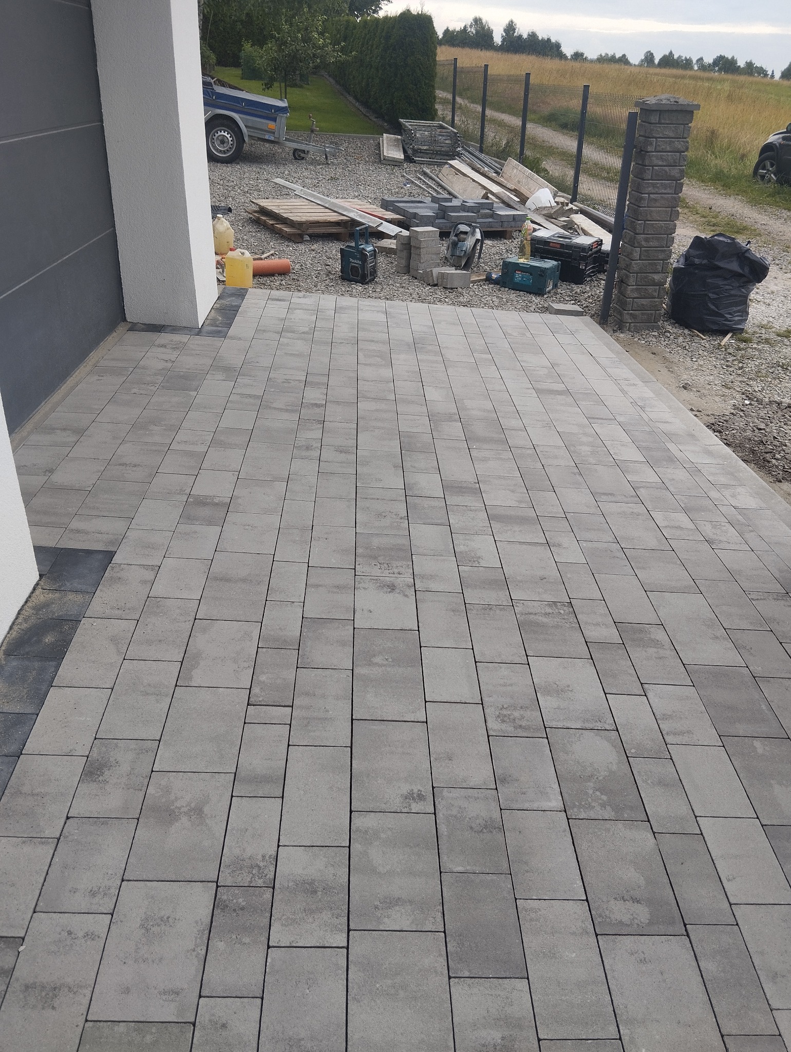 Nowo ułożona, szara kostka brukowa przed budynkiem z widocznymi narzędziami i materiałami budowlanymi w tle.