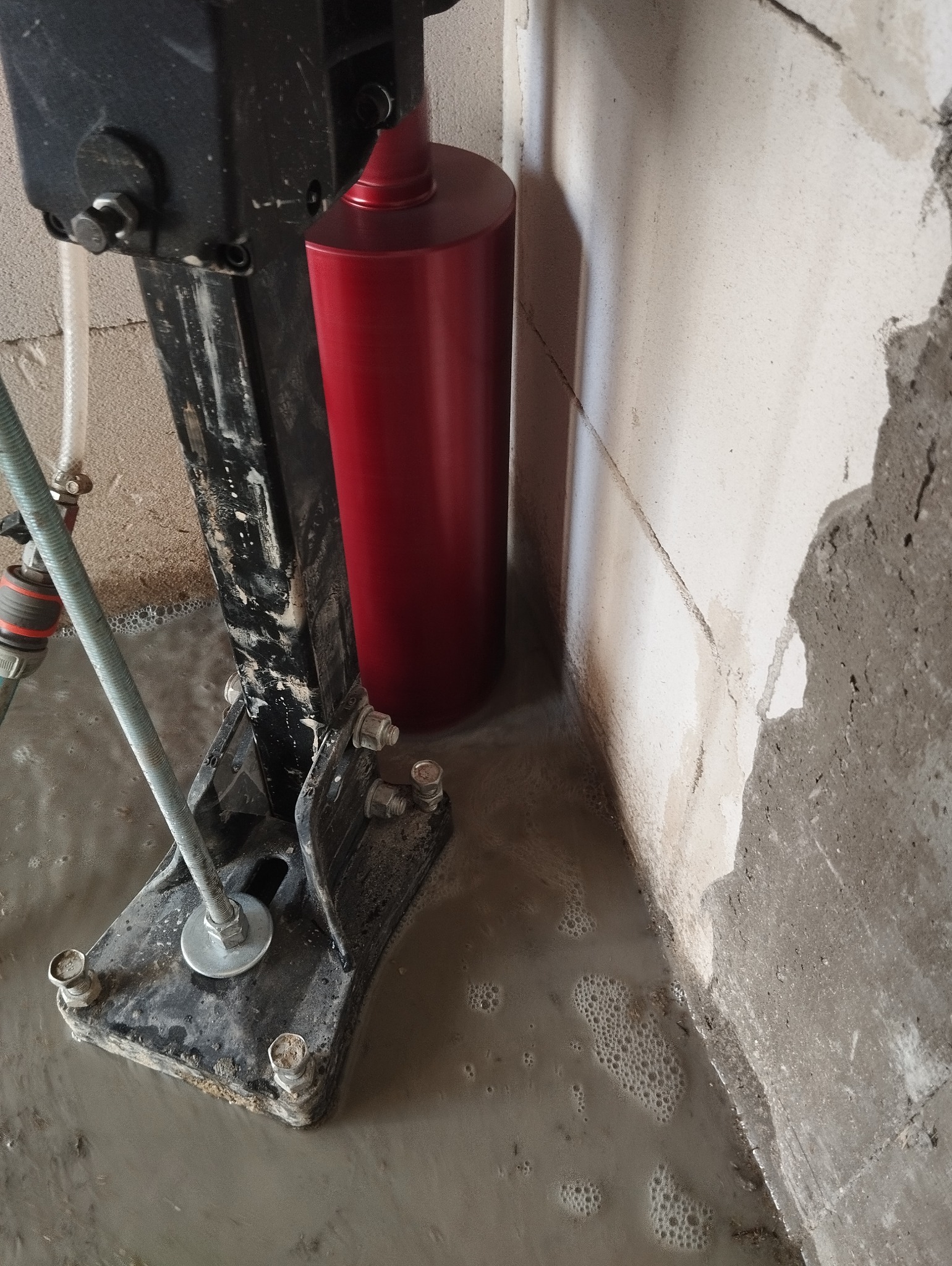 Wiertnica diamentowa rdzeniowa podczas pracy: czerwony cylinder wiertła, woda chłodząca, wiercenie w ścianie z betonu komórkowego.