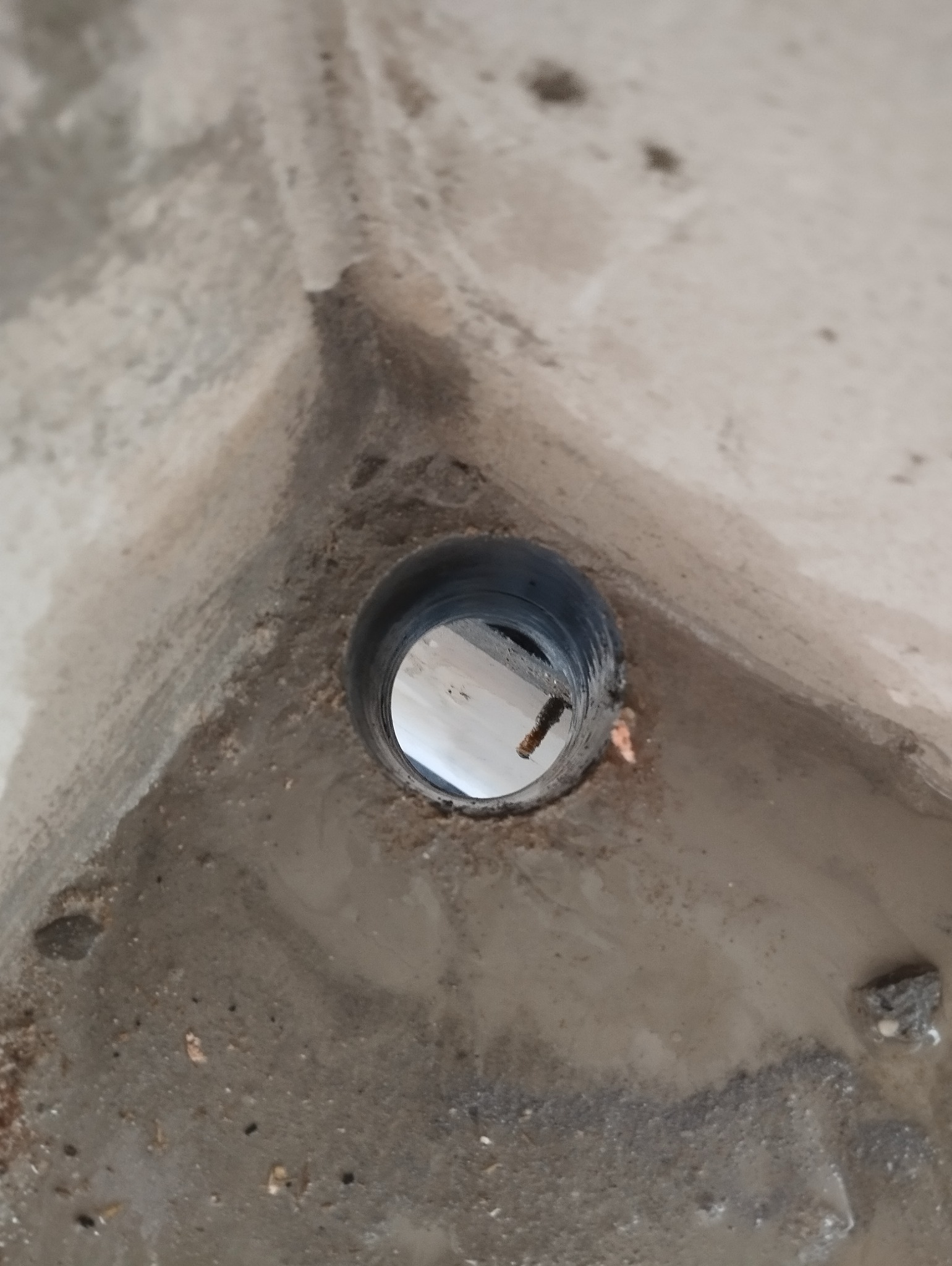 Otwór w betonowej ścianie z widocznym elementem instalacji wewnątrz, prawdopodobnie przygotowanie do montażu rury.