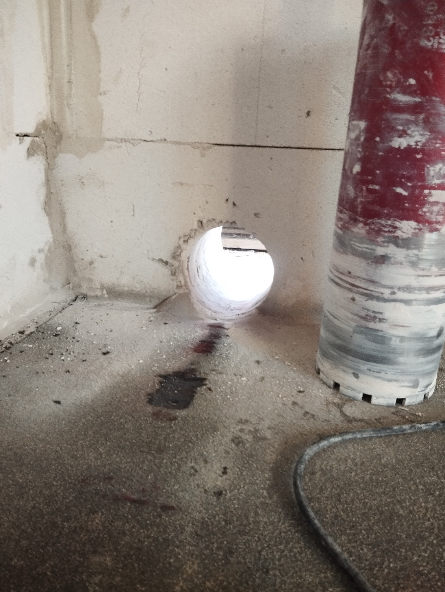 Wywiercony otwór w ścianie z betonu komórkowego, widoczny rdzeń wiertniczy obok, ślady wiercenia na podłodze.