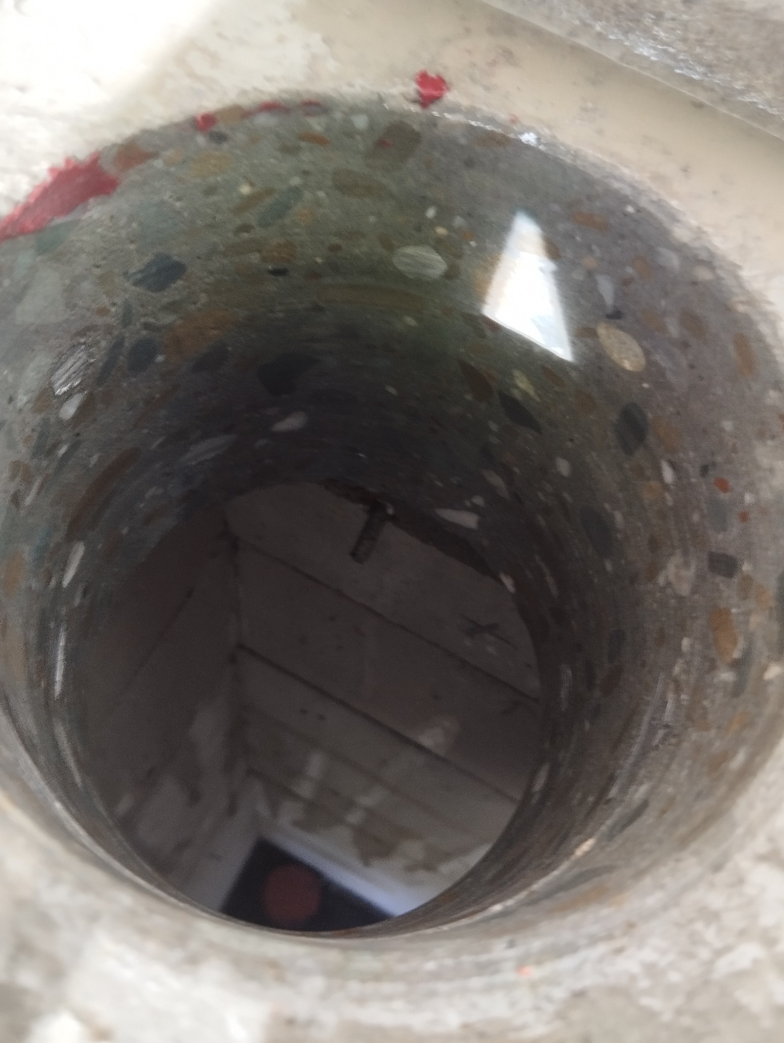 Wnętrze betonowej studni z wodą, widoczne drewniane elementy konstrukcyjne na dnie, perspektywa z góry.