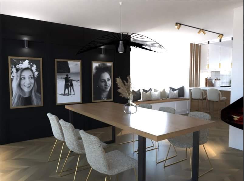 Jadalnia w stylu nowoczesnym z drewnianym stołem, krzesłami na złotych nogach, czarną ścianą z trzema oprawionymi zdjęciami i oryginalną lampą wiszącą.