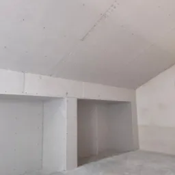 Pokój w trakcie wykańczania, widoczne ściany i sufit pokryte szarą płytą, przygotowane wnęki na szafy w zabudowie, szpachlowane łączenia płyt.
