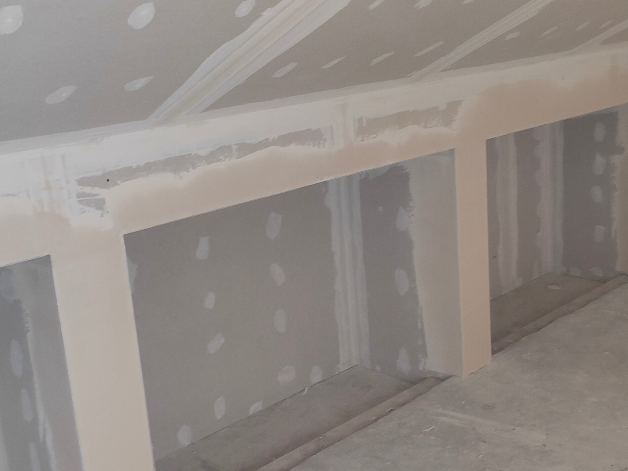 Wnętrze w trakcie wykańczania z widocznymi wnękami w ścianie i sufitem pod skosem, gdzie widoczne są miejsca po wkrętach i szpachlowaniu.