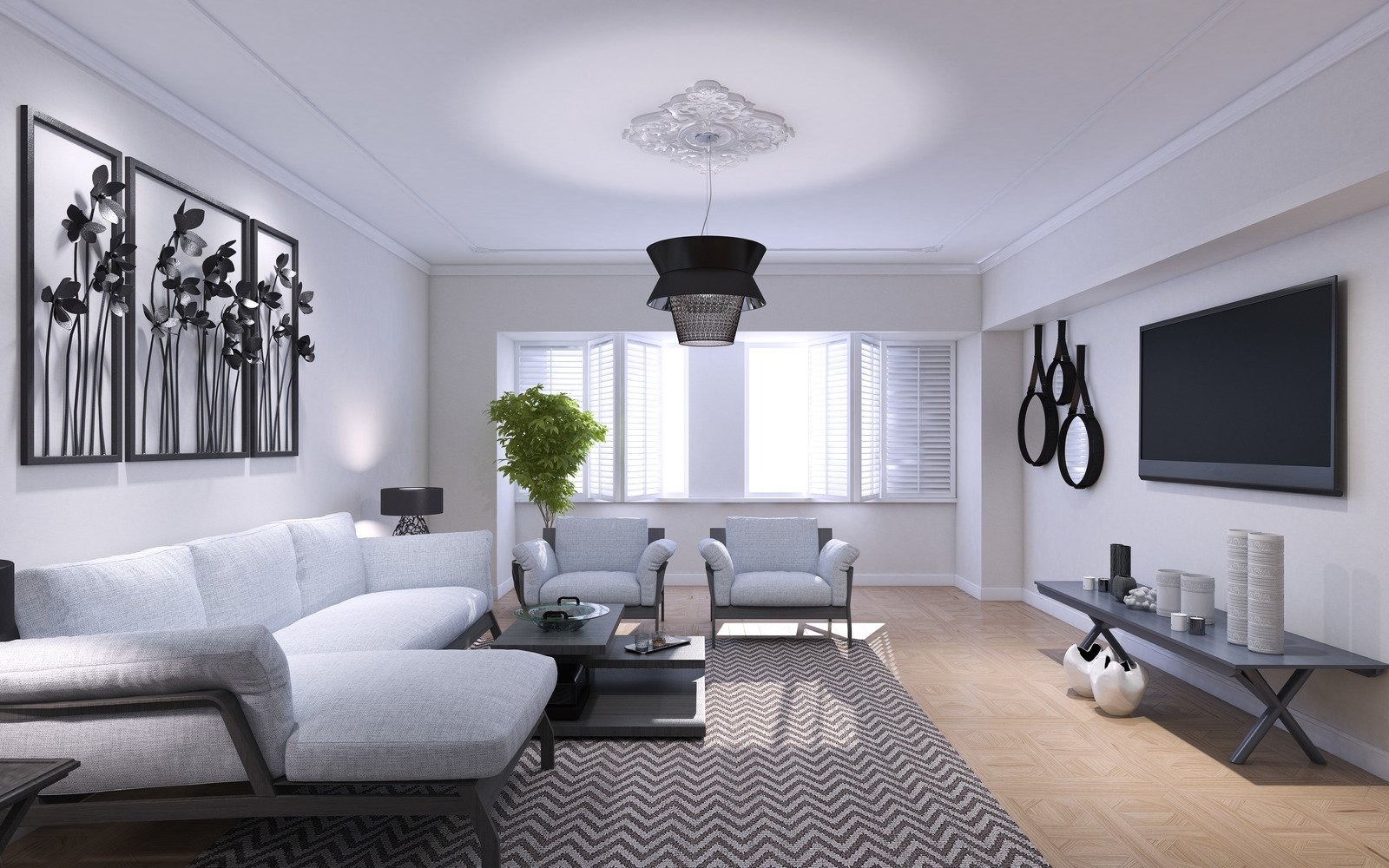 Jasne wnętrze salonu z szarą sofą narożną, dwoma fotelami, wzorzystym dywanem i dekoracjami ściennymi w postaci metalowych kwiatów oraz luster w czarnych oprawach, oświetlone nowoczesną lampą wiszącą.