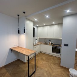 Myroslav Holembiovskiy - Nowoczesna kuchnia z białymi szafkami, drewnianym blatem i podłogą ułożoną w jodełkę, uzupełniona o minimalistyczne lampy wiszące i drewniany blat przymocowany do ściany.