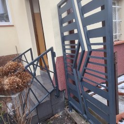 Antex Damian Brzozowski - Nowoczesna, szara balustrada metalowa z poziomymi szczeblami, zamontowana przy schodach wejściowych do domu, z widocznymi śladami wilgoci na powierzchni.