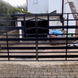Antex Damian Brzozowski - Czarna, metalowa brama wjazdowa dwuskrzydłowa z automatyką, zamontowana na ceglanych słupkach, widok z zewnątrz posesji.