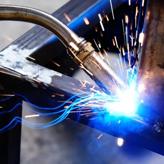 Proces spawania metalowych profili, widoczne iskry i intensywne światło łuku elektrycznego, zbliżenie na uchwyt spawalniczy.