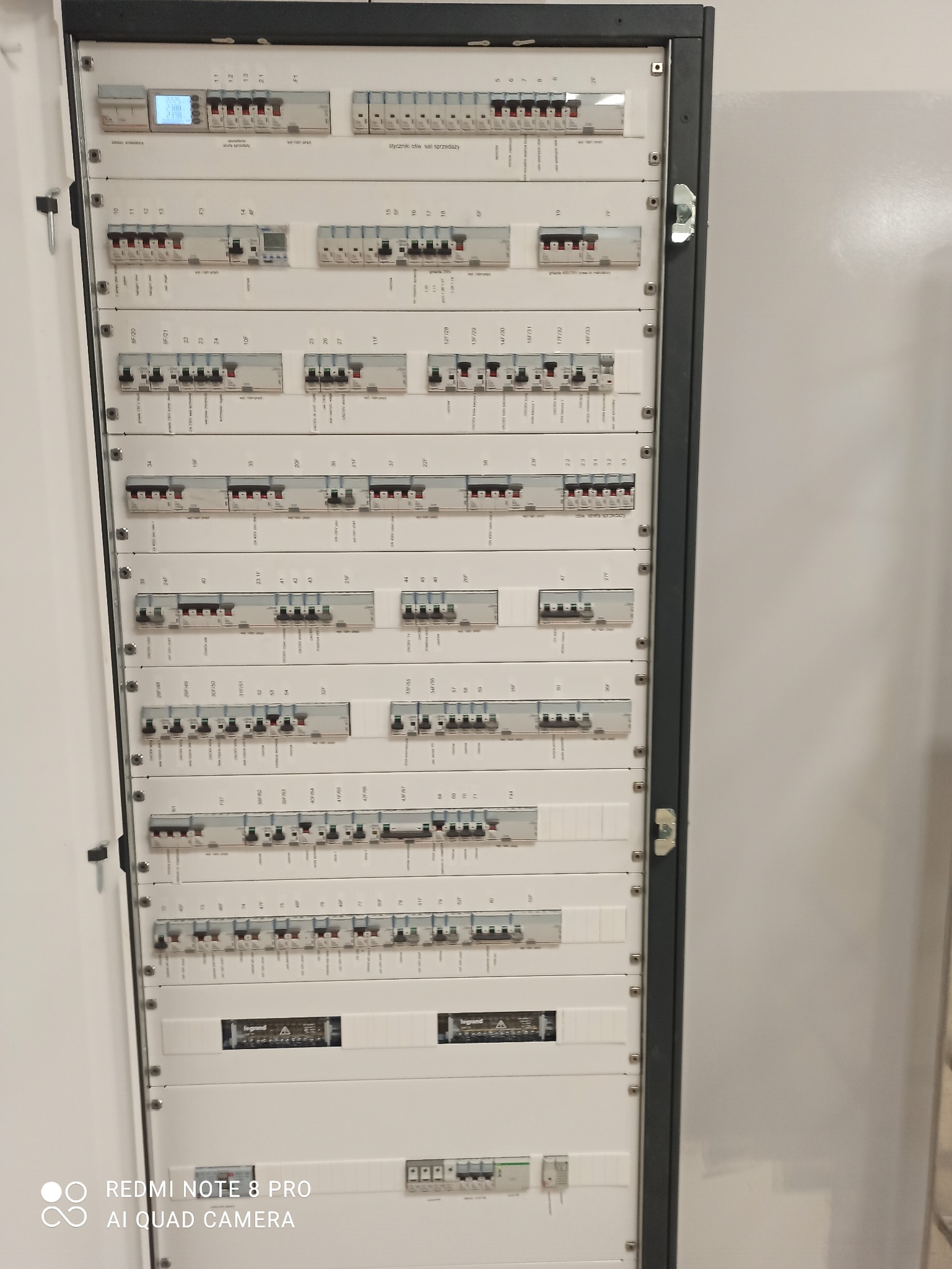 Rozdzielnica elektryczna z wieloma zabezpieczeniami nadprądowymi i różnicowoprądowymi, widok z bliska na otwartą szafę, z widocznymi opisami obwodów i elementami marki Legrand.