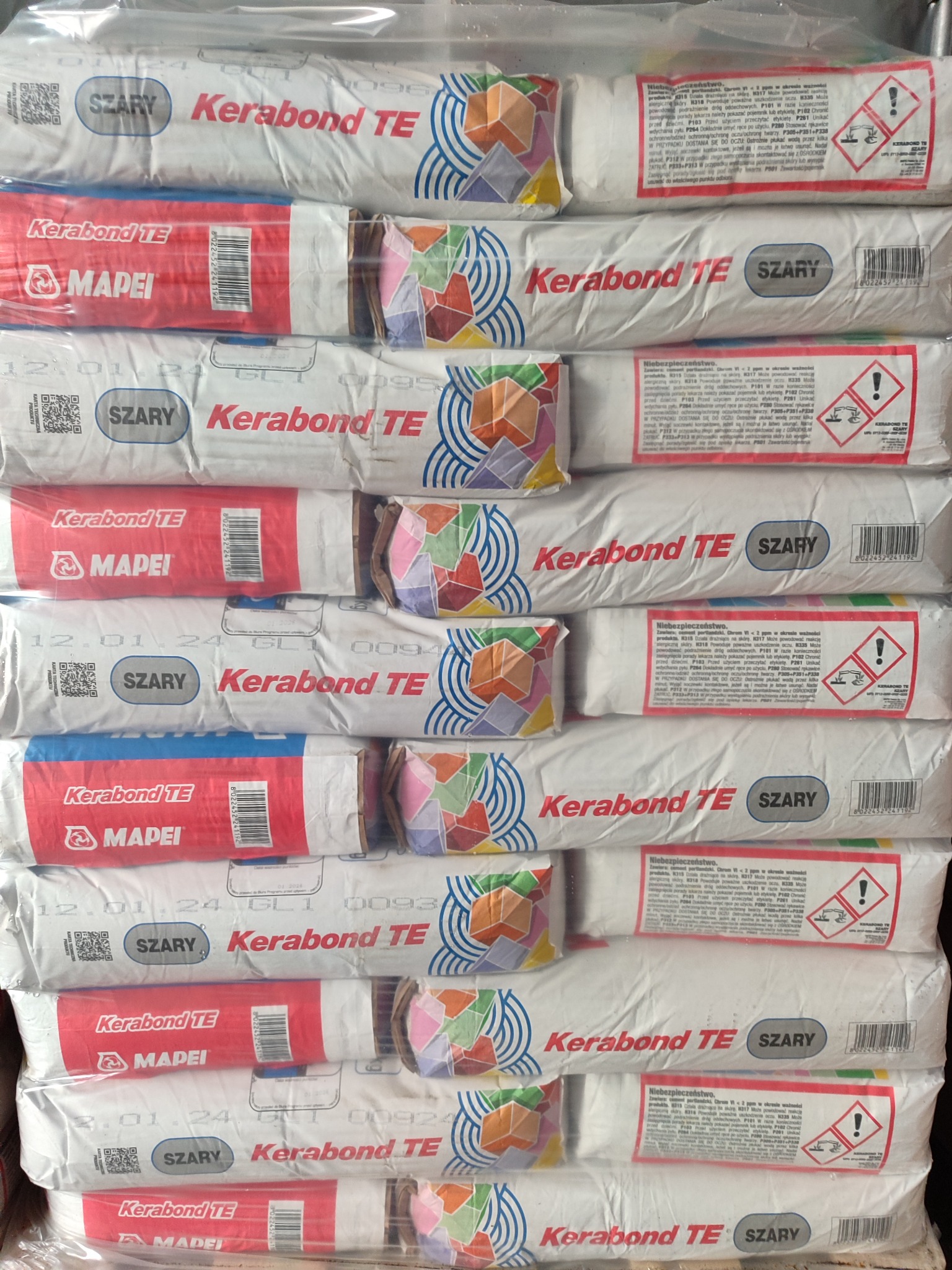 Stos ułożonych jeden na drugim worków z zaprawą klejową Kerabond TE Szary firmy Mapei, zapakowanych w przezroczystą folię.