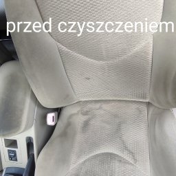 CZYSTY DOM I SAMOCHÓD - MARCIN KWAPISZ - Tapicerka fotela samochodowego z widocznymi plamami i zabrudzeniami przed procesem czyszczenia, widok z góry na fotel kierowcy, z fragmentem kierownicy w dolnej części kadru.