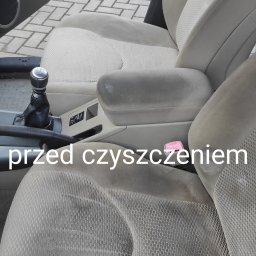 CZYSTY DOM I SAMOCHÓD - MARCIN KWAPISZ - Brudna, jasna tapicerka fotela samochodowego z widocznymi plamami i zabrudzeniami, przed praniem. Widoczny fragment deski rozdzielczej z dźwignią zmiany biegów.