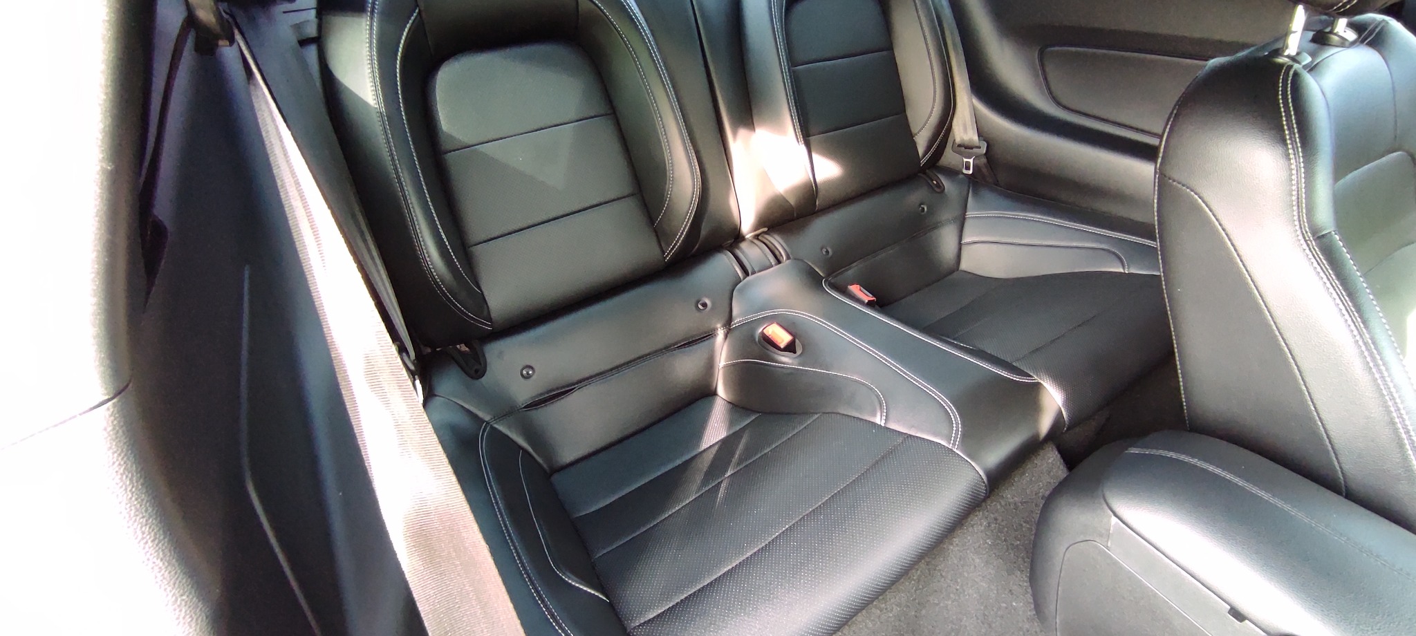 Czarne skórzane tylne siedzenia samochodu z białymi przeszyciami i widocznymi pasami bezpieczeństwa.