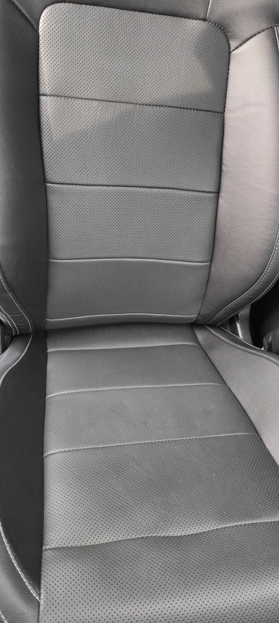 Czarne, perforowane skórzane siedzisko samochodowe z jasnymi przeszyciami, widok z góry, ukazujące detale faktury i szwów.