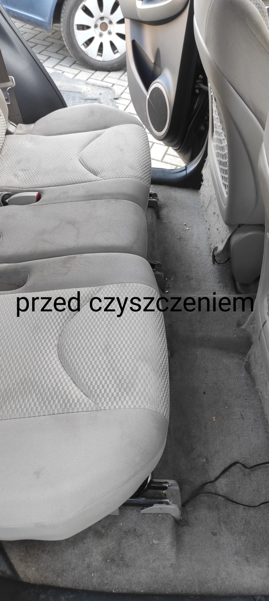 Wnętrze samochodu z widocznymi, zabrudzonymi siedzeniami i podłogą przed czyszczeniem, z bliska widoczna teksturowana tapicerka.