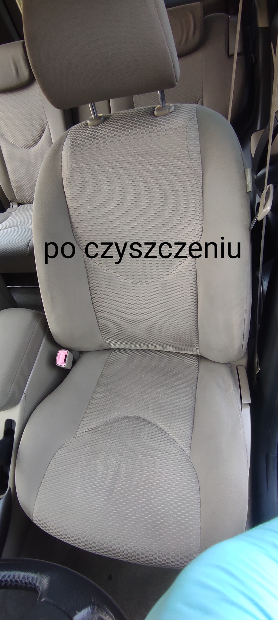 Szare, wyczyszczone siedzenie samochodowe z widocznym zagłówkiem i częścią pasów bezpieczeństwa, uchwycone z góry w pochmurnym oświetleniu.