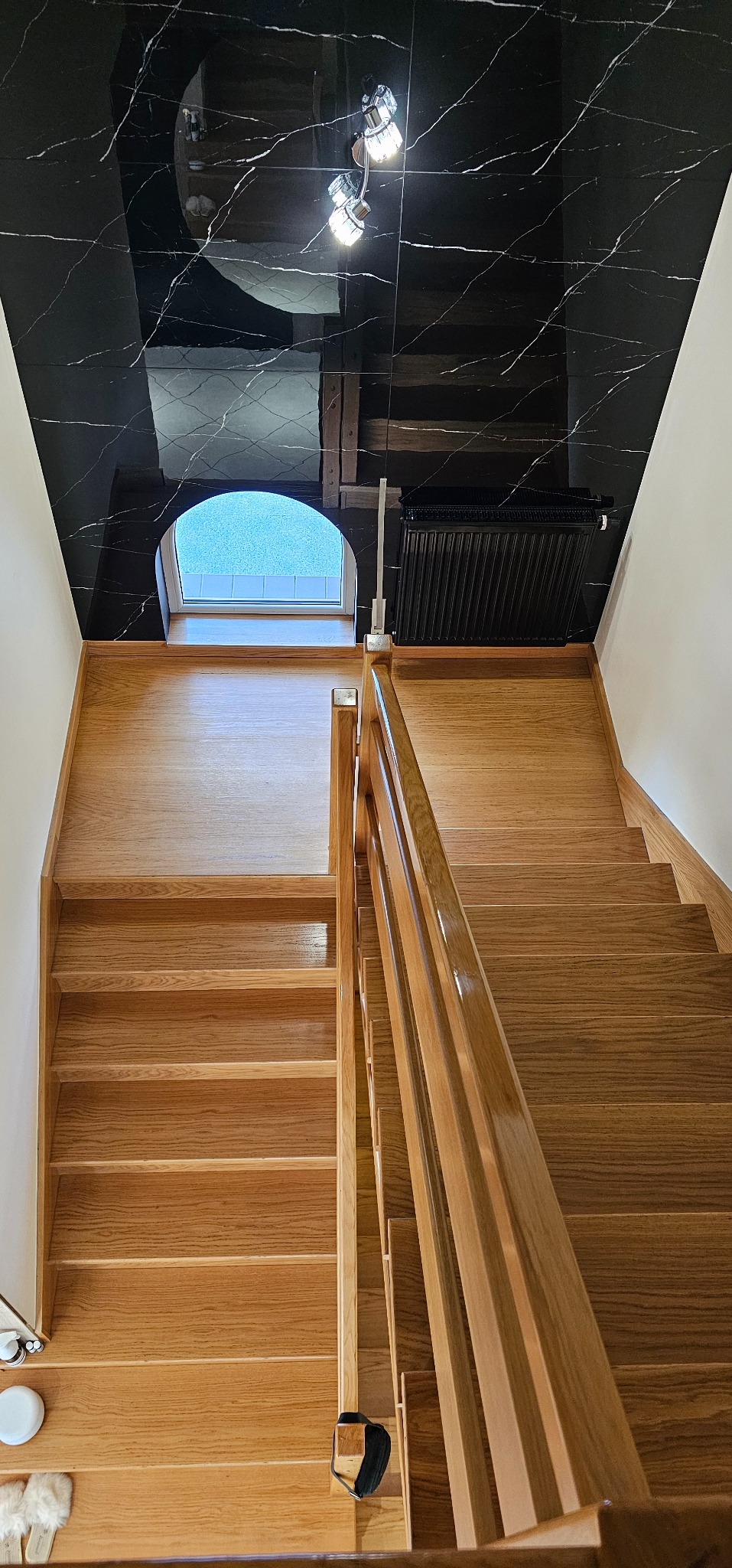 Drewniane schody z jasnego drewna, widok z góry, czarny sufit z marmurowym wzorem odbija światło, małe okno pod sufitem