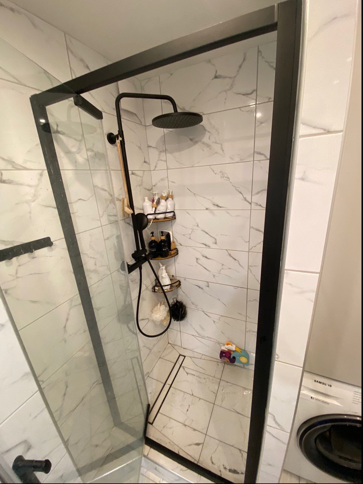 Nowoczesna kabina prysznicowa z czarną armaturą i marmurowymi płytkami w Bielsko-Białej, widok z boku, zabawka na podłodze.