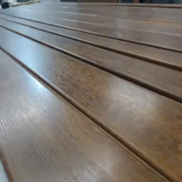 Brązowe, lakierowane profile metalowe z widoczną strukturą drewna, ułożone równolegle, prawdopodobnie elementy konstrukcyjne pergoli.