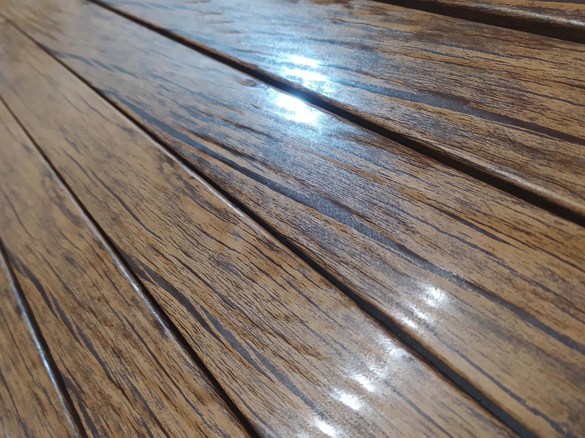 Szczegółowe ujęcie brązowych, drewnopodobnych paneli ogrodzeniowych ułożonych ukośnie, z widoczną teksturą i połyskiem lakieru.