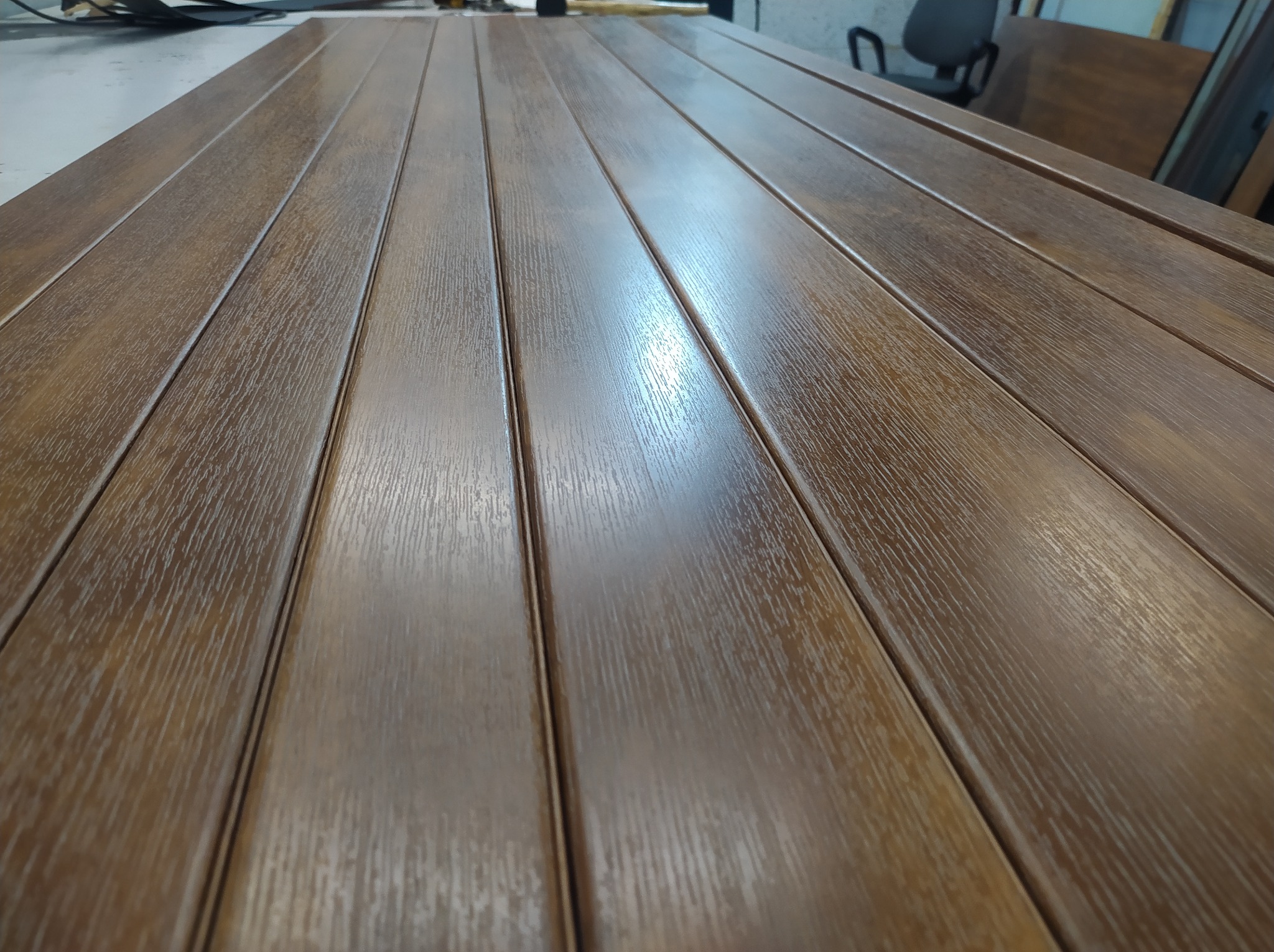 Panelowe elementy z brązowego metalu, prawdopodobnie fragment konstrukcji, z widoczną fakturą drewna i odbiciami światła.