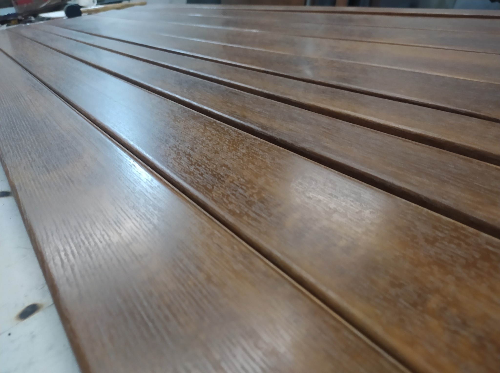 Brązowe, lakierowane profile metalowe z widoczną strukturą drewna, ułożone równolegle, prawdopodobnie elementy konstrukcyjne pergoli.