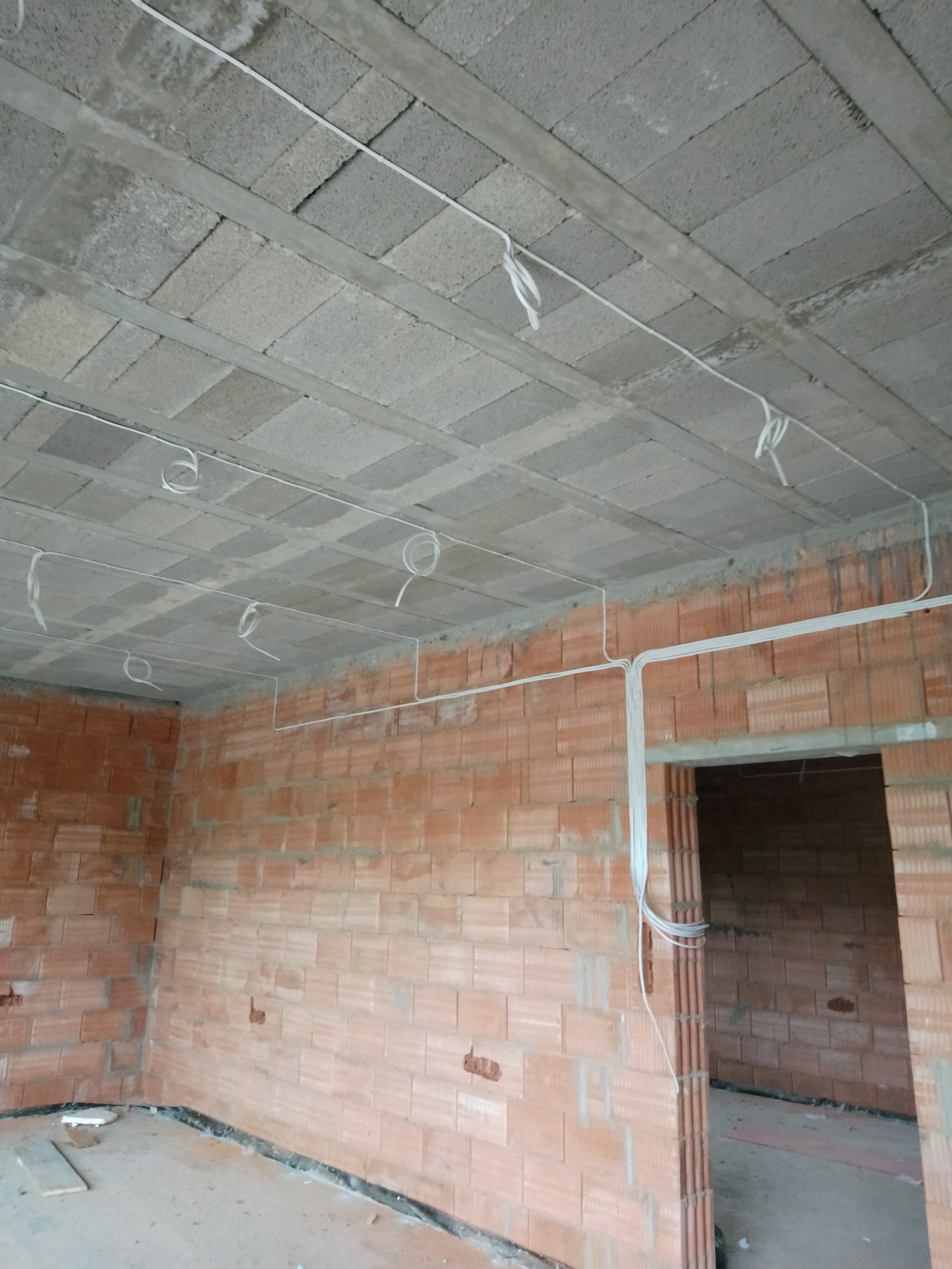 Wnętrze w stanie surowym: ceglane ściany i betonowy strop z widocznymi przewodami elektrycznymi, wstępna faza instalacji.