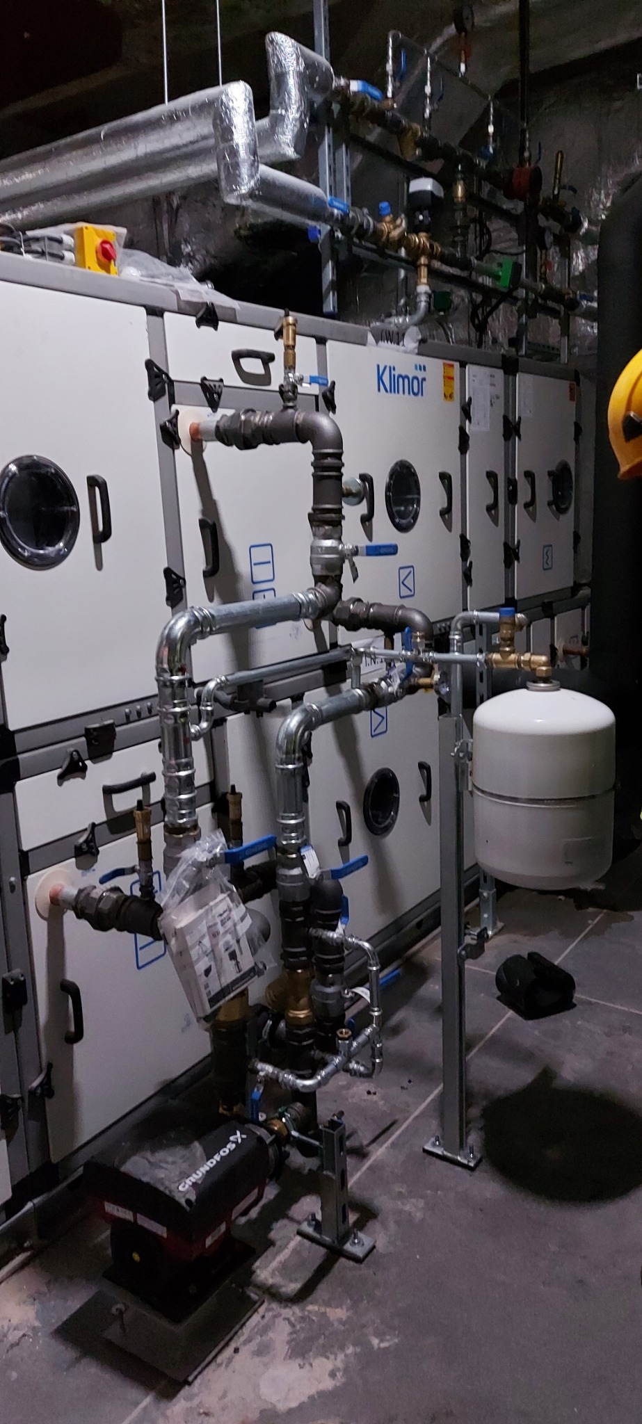 Instalacja grzewcza z pompą obiegową Grundfos i zbiornikiem wyrównawczym w kotłowni w Pobiedziskach, widoczne liczne rury i zawory.