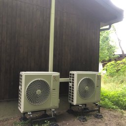 Ecowent - Dwa zewnętrzne agregaty klimatyzacji Rotenso zamontowane na czarnych podstawach na zewnątrz drewnianego budynku. Widoczne rury chłodnicze w kolorze jasnej zieleni.