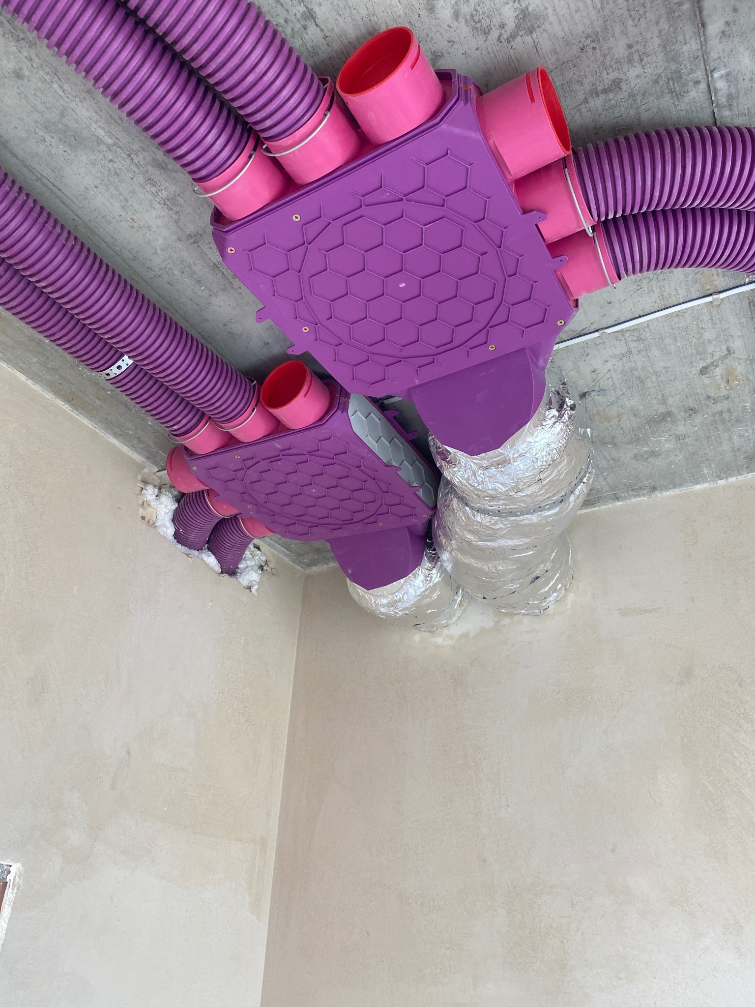 Fioletowe kanały wentylacyjne z rozdzielaczami o strukturze plastra miodu, zamontowane pod betonowym sufitem w pomieszczeniu w trakcie wykończenia.