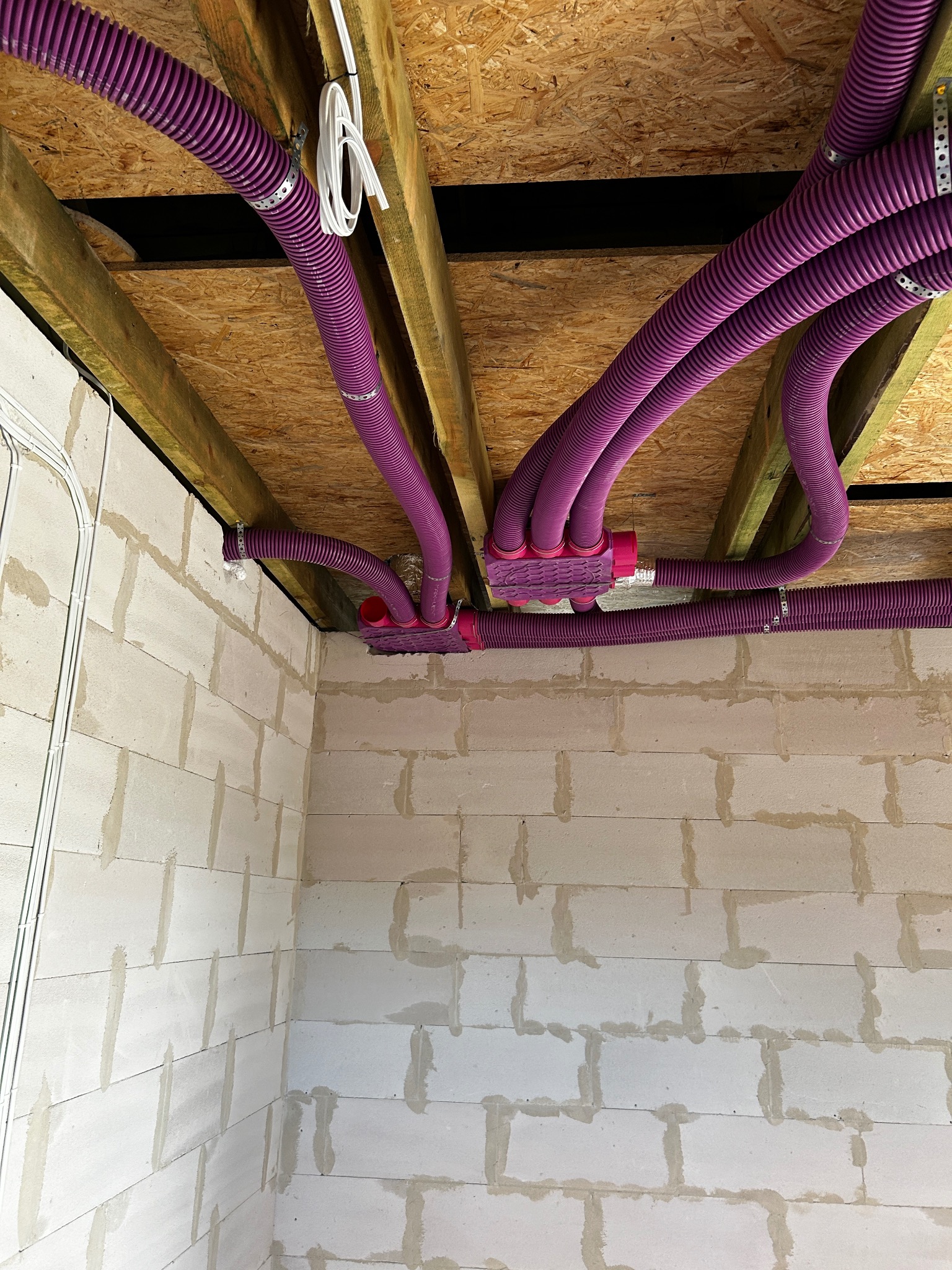 Fioletowe rury wentylacyjne przymocowane do drewnianej konstrukcji stropu w surowym wnętrzu budynku z białych bloczków.