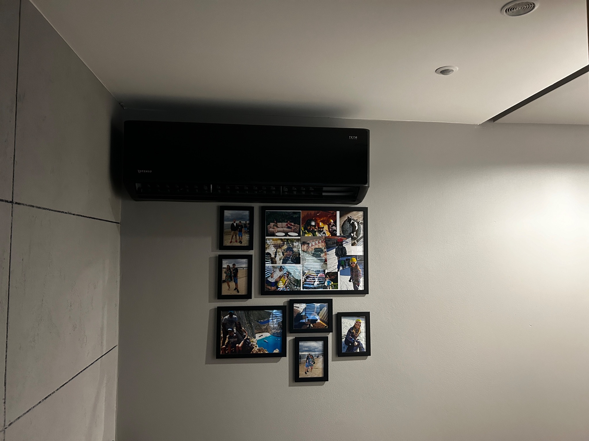 Czarna klimatyzacja Rotenso na szarej ścianie z galerią zdjęć w czarnych ramkach, widok z dołu.