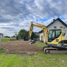 Szymon Czysz - Żółta koparka Hyundai 55-9 na działce w Mizerowie po wykonaniu prac ziemnych. W tle dom i pochmurne niebo. Widoczny wykop pod przyszłą budowę.