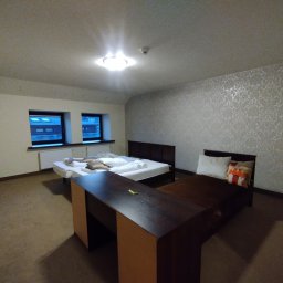 Jacek Bałuszyński LeoColor Usługi Malarsko-Wykończeniowe - Pokój hotelowy po odświeżeniu: dwie szafki nocne, dwa łóżka z pościelą, ściana z wzorzystą tapetą, dywan na podłodze. Widok na okna z widokiem na zewnątrz.