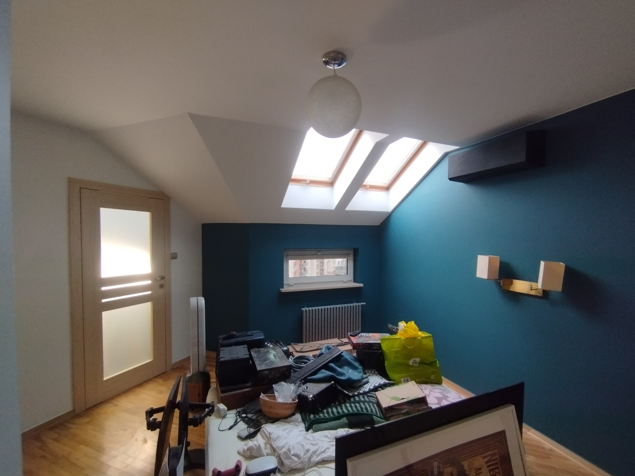 Pokój na poddaszu po odświeżeniu: turkusowa ściana, biały sufit z oknami dachowymi i lampą. Widoczny fragment zagraconego łóżka i drzwi z przeszkleniem.