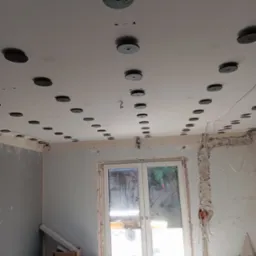 Przygotowanie do montażu sufitu napinanego: widoczne rozmieszczenie punktów mocowania na suficie z użyciem poziomicy laserowej, ściany częściowo przygotowane do dalszych prac wykończeniowych, worki...