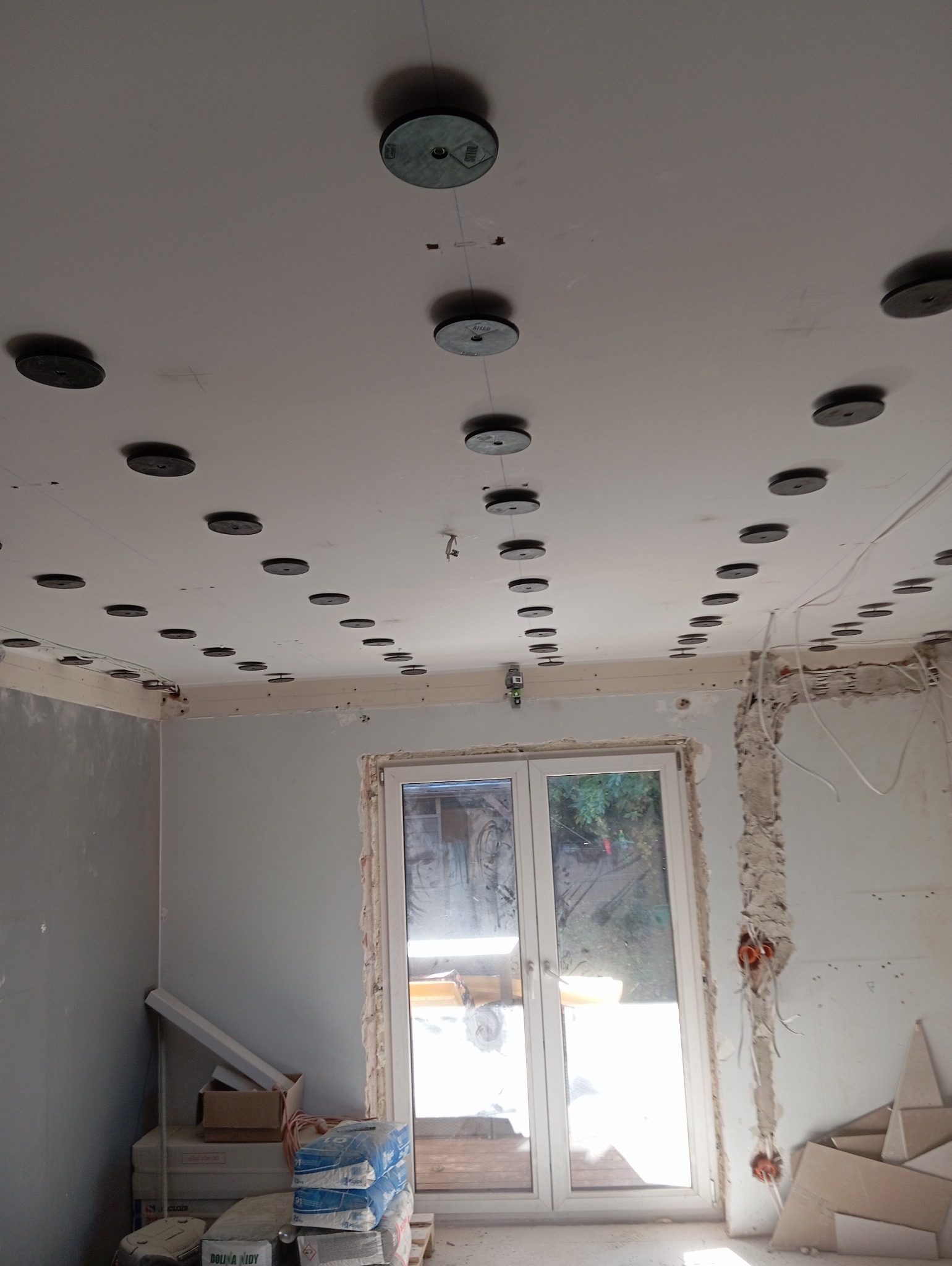 Przygotowanie do montażu sufitu napinanego: widoczne rozmieszczenie punktów mocowania na suficie z użyciem poziomicy laserowej, ściany częściowo przygotowane do dalszych prac wykończeniowych, worki...